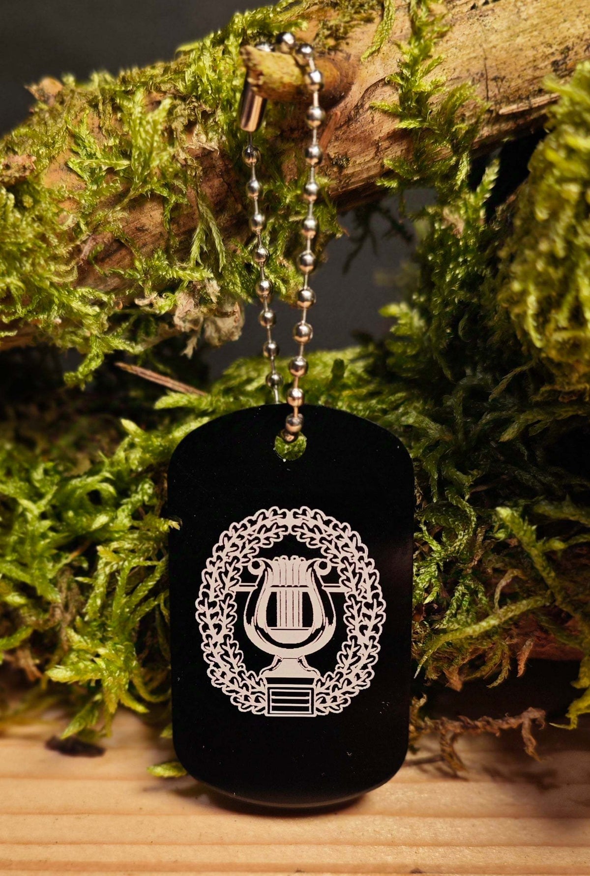 Anhänger Dog Tag aus schwarzer Aluminiumlegierung mit einer silbernen Gravur eines Lorbeerkranzes und einer Lyra, inklusive Kugelkette