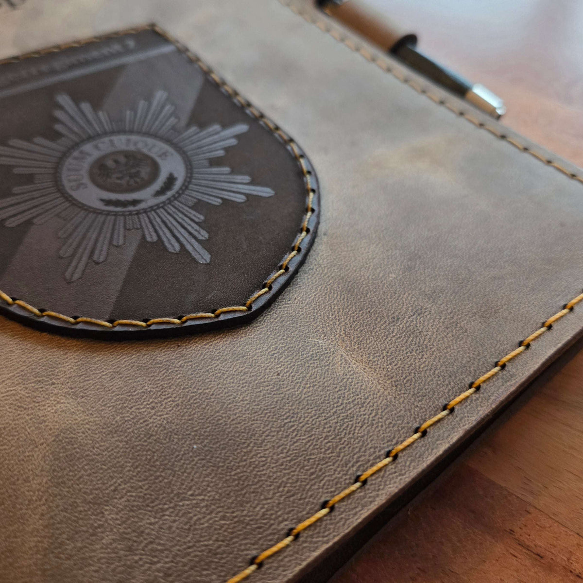 DIN A5 Organizer aus braunem Leder mit gelben Nähten, handgefertigtem Wappen und integriertem Stiftehalter in Schwarz