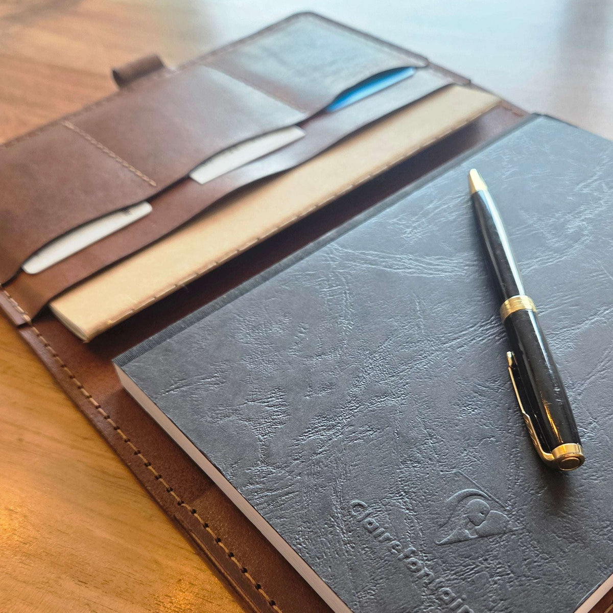 DIN A5 Organizer aus braunem Leder mit aufgeschlagenen Fächern, Notizbuch und schwarzem Kugelschreiber mit Goldakzenten