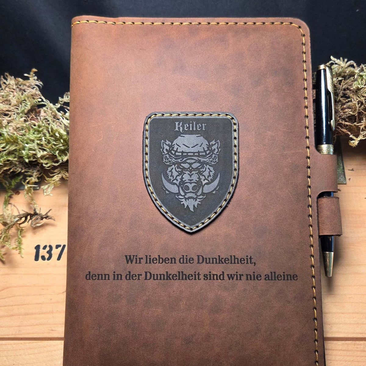 DIN A5 Organizer aus braunem Leder mit schwarzer Naht, aufgenähtem Wappen und graviertem Spruch