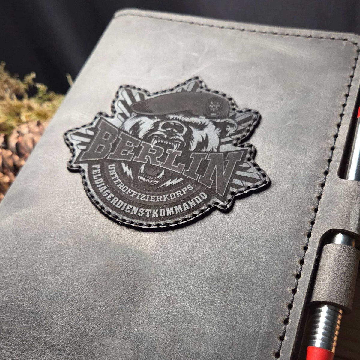 DIN A5 Organizer aus grauem Leder mit aufgenähtem Bundeswehr-Bergwacht-Wappen und schwarzem Stiftehalter