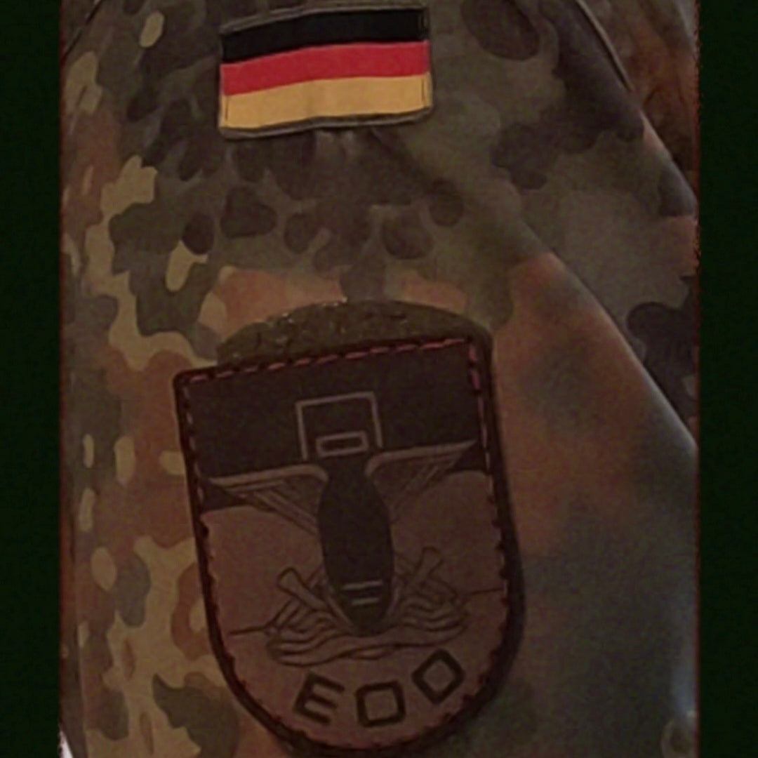 EOD Leder Patch aus braunem Echtleder mit graviertem Symbol einer Bombe, angedeuteten Blitzen und Schutzschild auf Tarnuniform