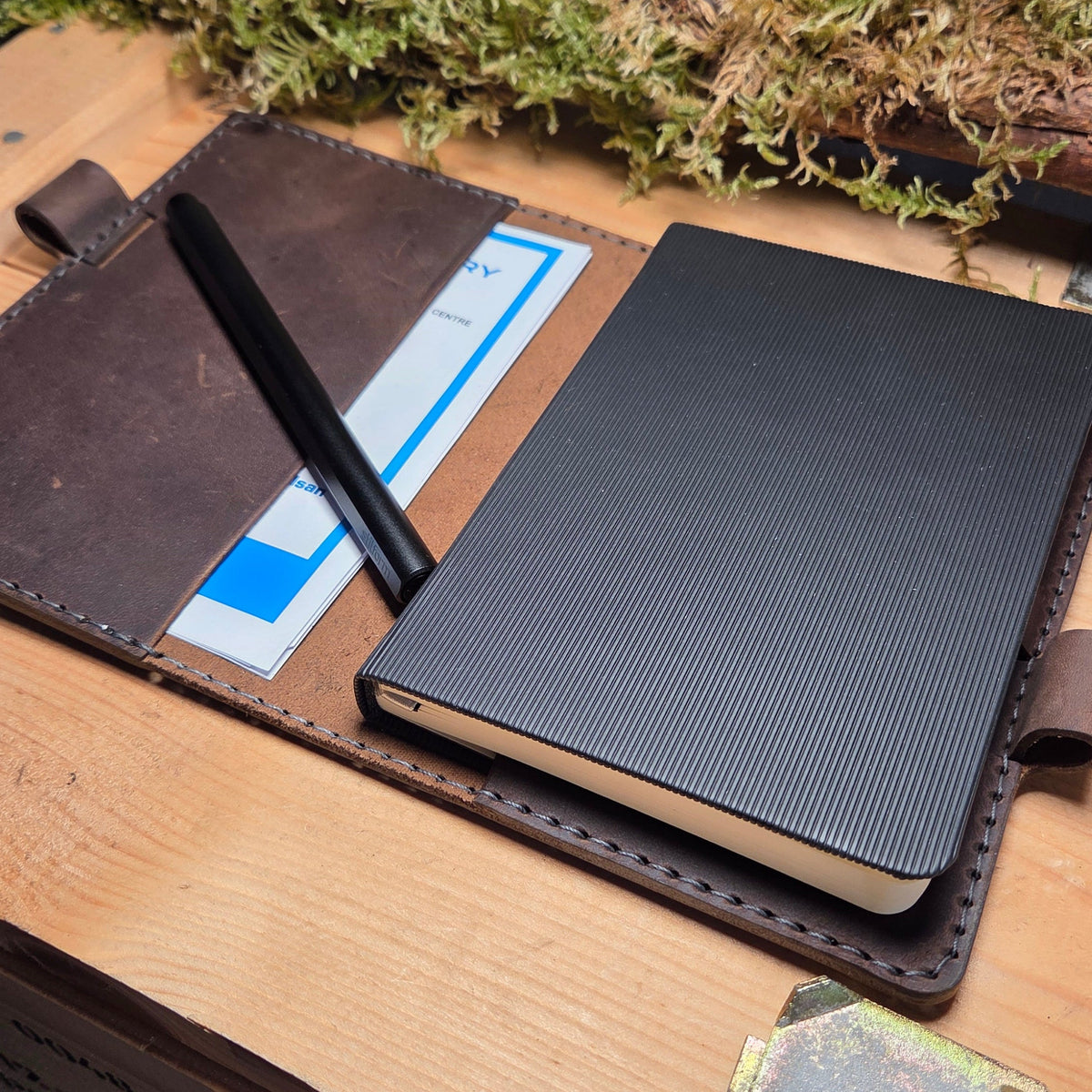 Handgefertigter Premium DIN A6 Organizer aus braunem Leder mit Stiftehalter und Fächern, offen liegend mit Notizbuch und Stift