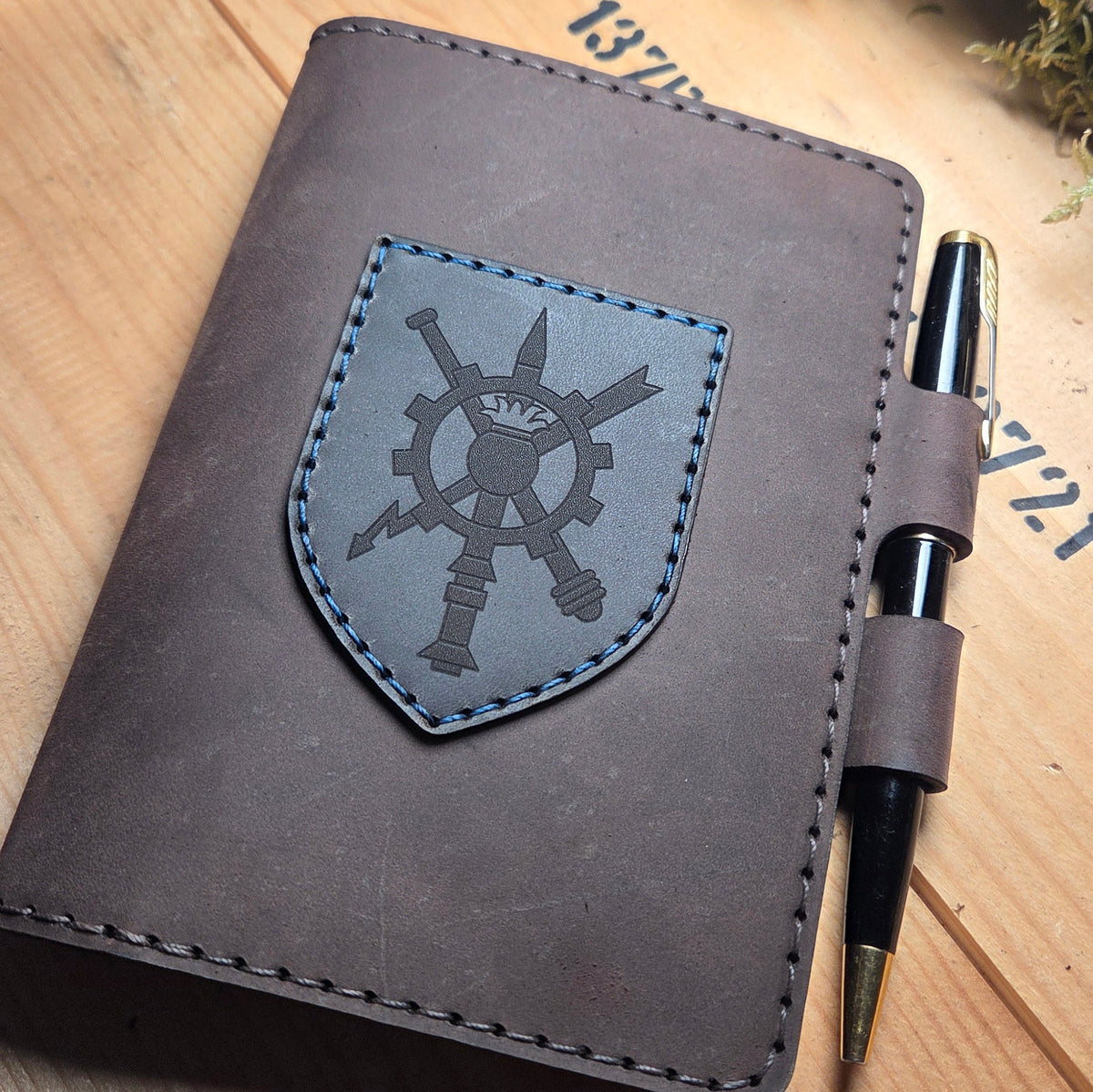 Handgefertigter Premium DIN A6 Organizer aus braunem Leder mit graviertem Wappen und blauem Zierstich, inklusive Stiftehalter