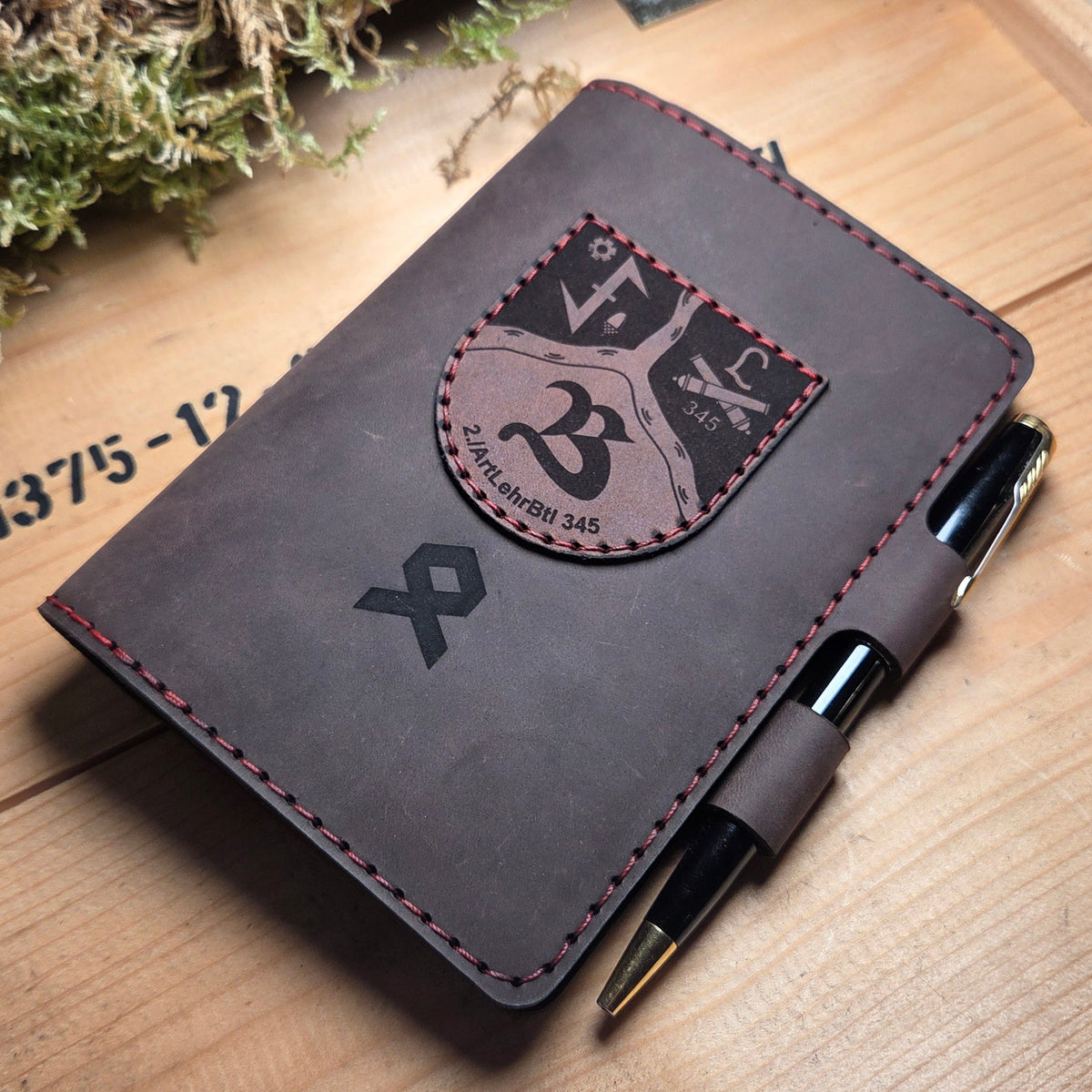 Handgefertigter Premium DIN A6 Organizer aus braunem Leder mit roter Naht, aufgenähtem Wappen und integriertem Stiftehalter