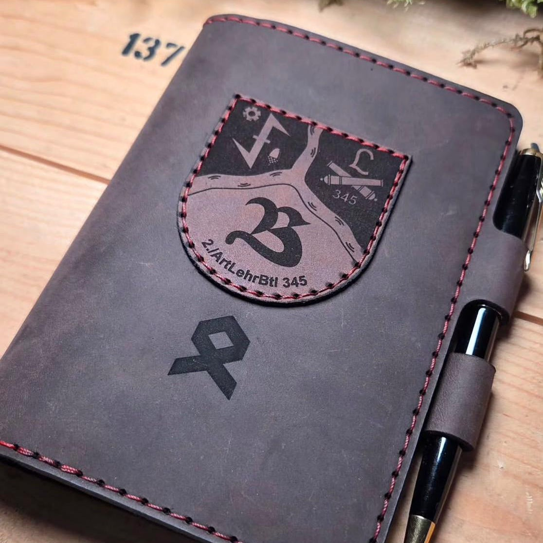 Handgefertigter Premium DIN A6 Organizer aus dunkelbraunem Leder mit roter Naht, aufgenähtem Wappen und integriertem Stiftehalter