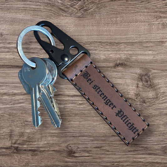 Individueller Lederanhänger aus braunem Vollnarbenleder mit schwarzer Naht und Gravur 'Bei strenger Pflicht', mit schwarzem Karabiner und Schlüsselring