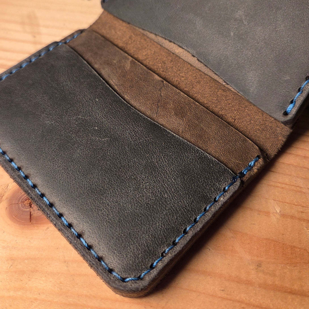 Kompaktes Leder-Wallet in dunkelgrauem Vollnarbenleder mit blauen Nähten und braunem Innenfutter aus Wildleder