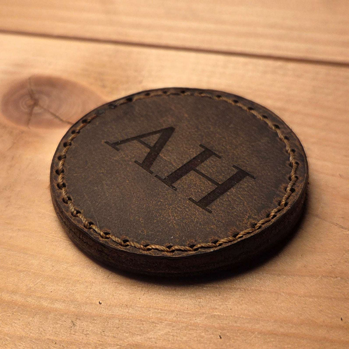 Runde Leder Coinhülle in braun mit handvernähtem Rand und individueller Gravur der Initialen AH auf der Oberfläche