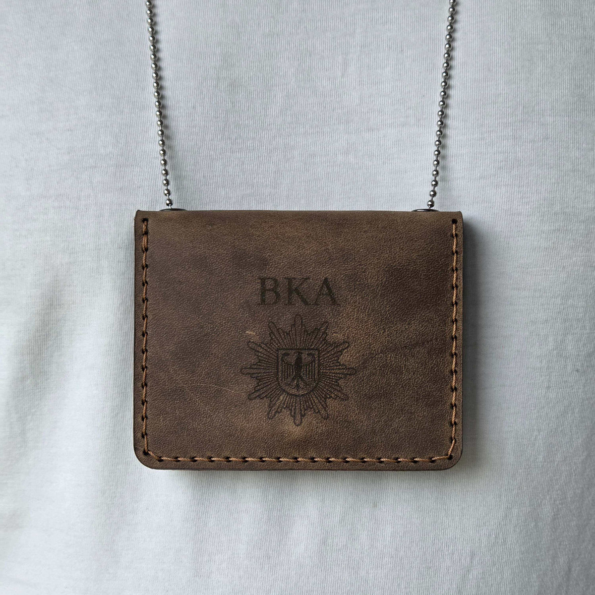 Leder-Dienstausweisetui aus dunkelbraunem Leder mit sichtbaren Nähten, BKA-Gravur und angehängter Metallkette