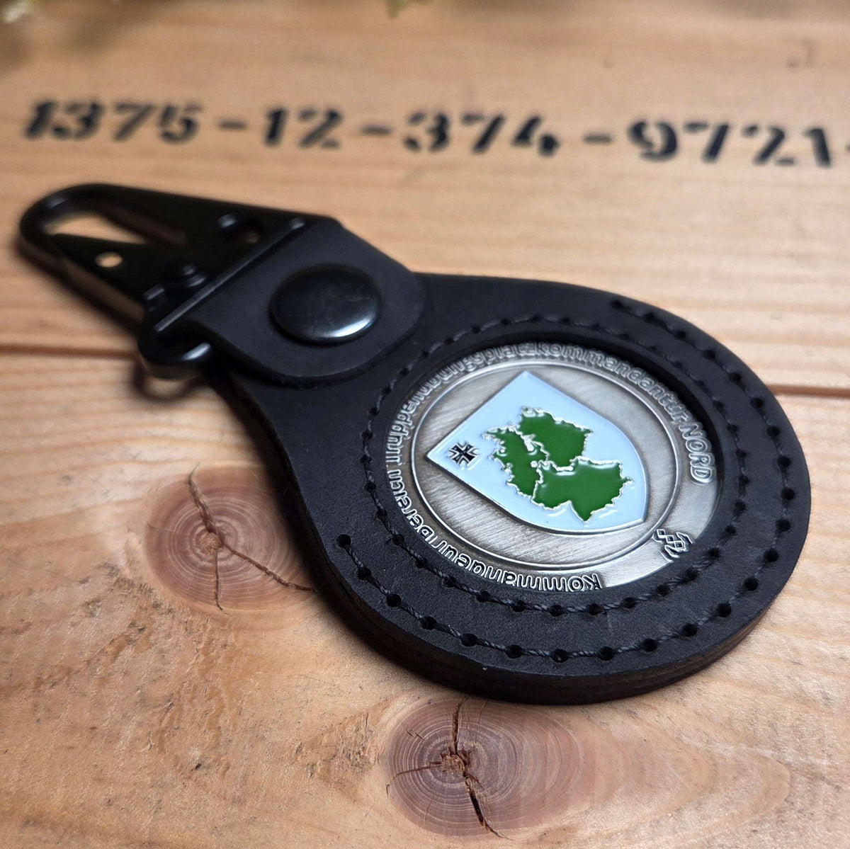 Lederanhänger für Challenge Coin aus schwarzem Leder mit sichtbarem silbernen Coin und grünem Motiv, Karabinerbefestigung