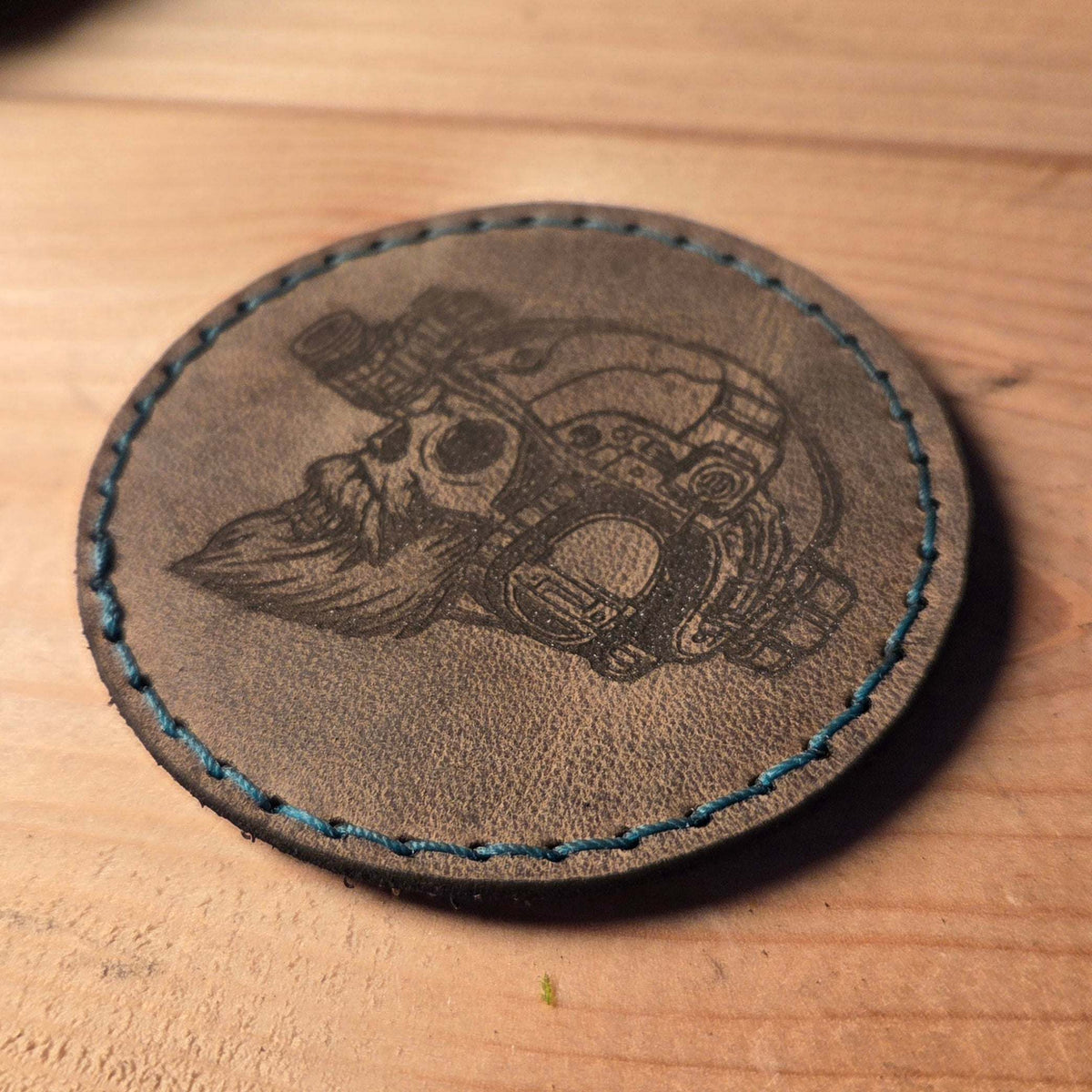 Runder brauner Lederpatch mit individueller Gravur einer Totenkopf-Grafik und blauer Handnaht aus Polyestergarn