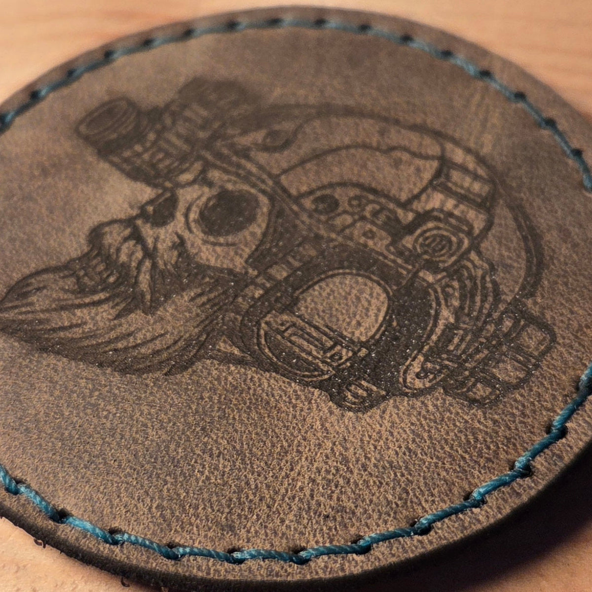Runder Lederpatch mit individueller Gravur in dunkelbraunem Büffelleder, handvernäht mit blauem Polyesterfaden, detailreiche Totenkopfzeichnung