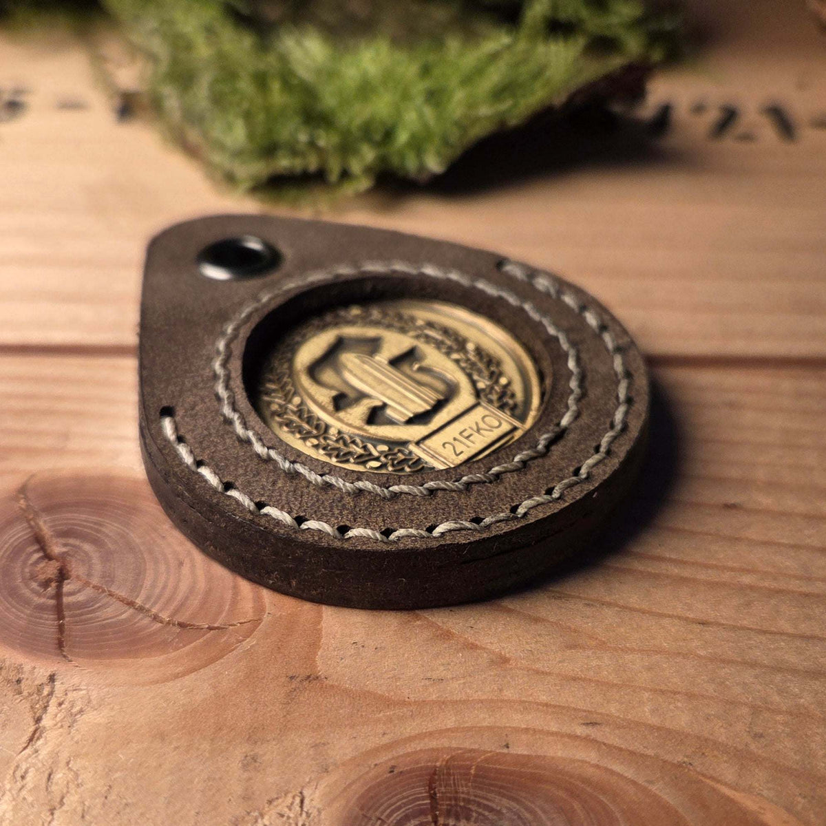 Schlüsselanhänger aus Leder in brauner Farbe mit handgenähtem Detail und eingearbeitetem Challenge Coin in der Mitte