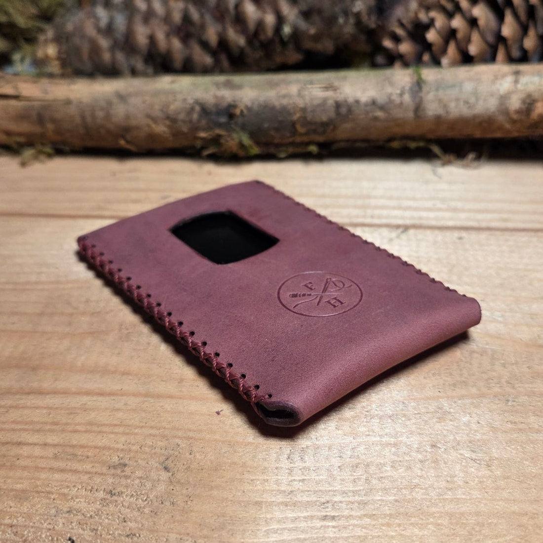 Slim Wallet aus Leder in dunklem Violett mit matter Oberfläche, umlaufender Handnaht und praktischem Kartenauswurf-Fenster