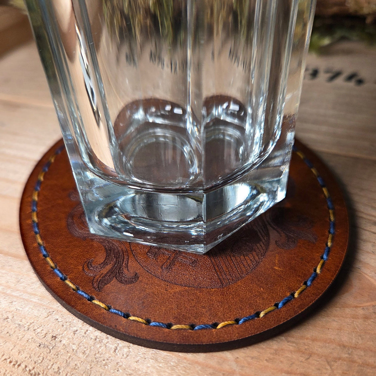 Untersetzer aus Leder in braunem Vollnarbenleder mit dekorativer Lasergravur und zweifarbiger blauer und gelber Naht am Rand